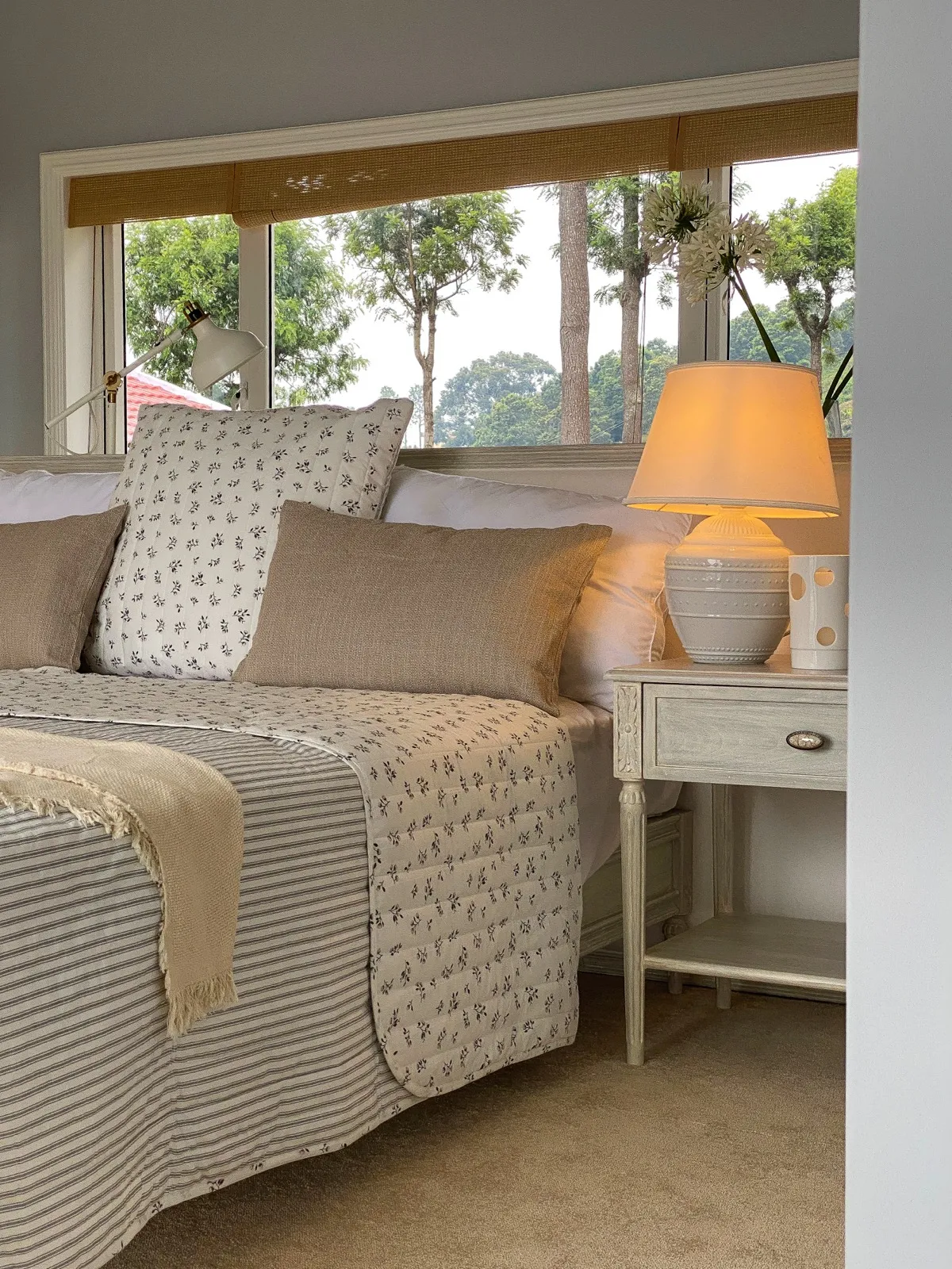 A dressed bed with a lamp and trees through the window at Coonoor by Sonia Gehlot